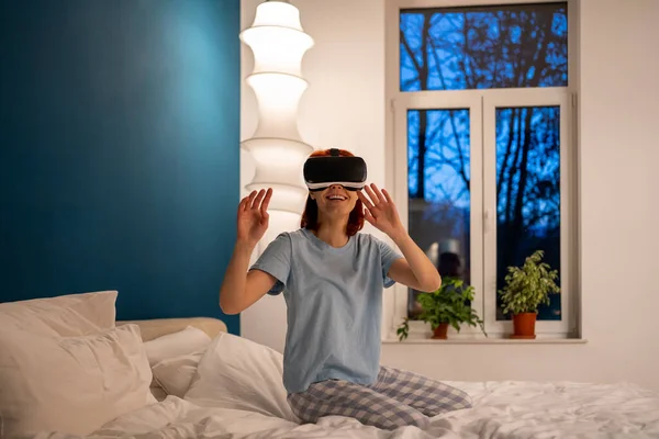 女人在床上用虚拟现实眼镜回家 女孩通过特殊装置 头盔模拟器玩电子游戏 快乐的女性戴着特殊的眼镜去探索不真实的世界 — 图库照片