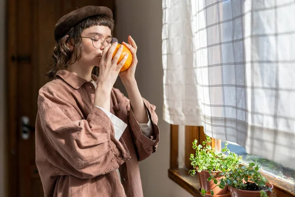 Millennial Dívka Vonící Oranžové Zavřenýma Očima Zatímco Stojí Okna Doma — Stock fotografie