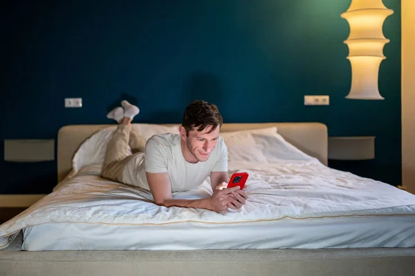 Homem Lendo Informações Smartphone Deitado Cama Casa Quarto Moderno Noite — Fotografia de Stock