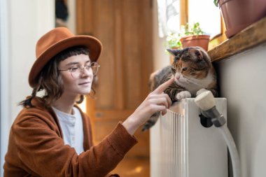 İnsan-kedi iletişimi. Mutlu gülümseyen genç kız evde kedisiyle oynuyor, evcil hayvanın burnuna dokunuyor, evcil hayvan sahibi olmanın tadını çıkarıyor. Evcil hayvanlar ve stres giderme kavramı