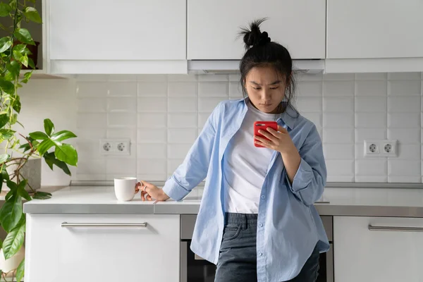 Молода Азіатка Стоїть Кухні Тримає Мобільний Телефон Читає Неприємні Смс — стокове фото