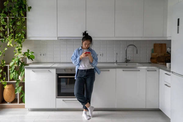 Chinesisches Mädchen Mit Mobiltelefon Während Einer Modernen Küche Mit Zimmerpflanzen — Stockfoto