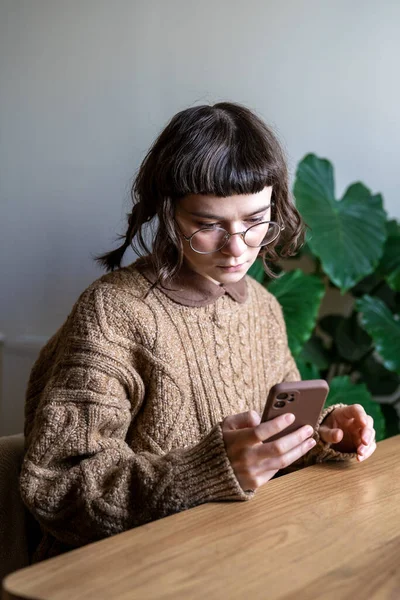 안경을 생각깊은 여자는 탁자에 스마트폰으로 네트워크 뉴스를 전화로 메시지를 네트워크를 — 스톡 사진