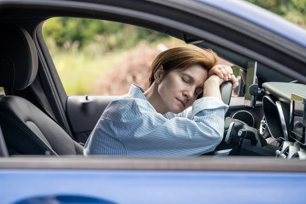ハンドルで眠っている中年疲れた女性は 長距離走行で疲れ果てた 女性ドライバーは 高速道路で休憩する疲れを感じています 車で旅行する 長距離の旅 — ストック写真