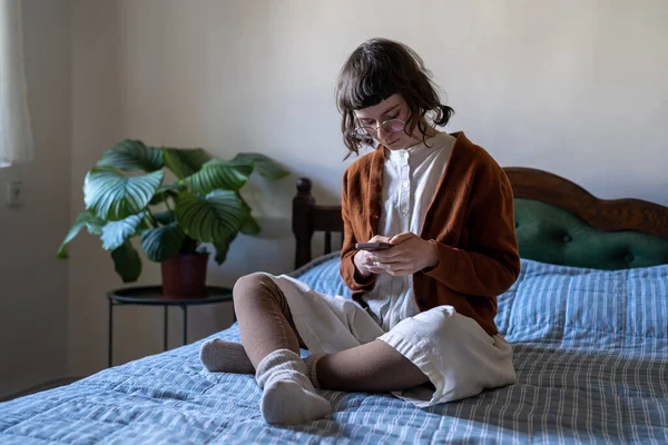 Pensive Marzycielska Studentka Siedzi Skrzyżowana Łóżku Patrząc Ekran Smartfona Czytając — Zdjęcie stockowe