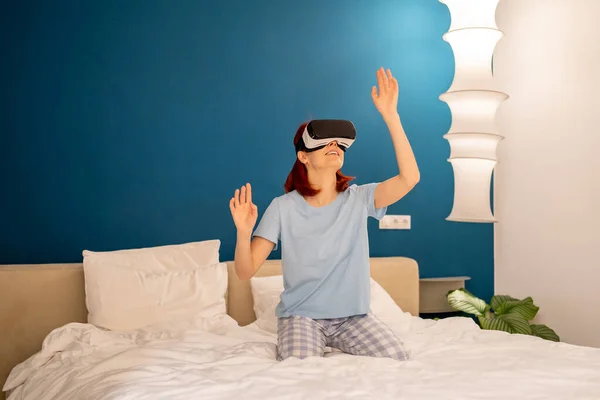 兴奋的笑着的女人戴著虚拟眼镜看电影玩游戏 高加索女性穿着Vr头盔坐在床上看着虚拟世界 网络空间 娱乐概念 — 图库照片