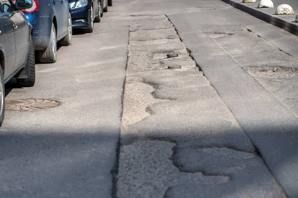 Şehirdeki asfalt yolda kırık ve park yerinde zamansız onarım. Çukur asfalt yol tamiri. Yamalı yol kötü durumda. Şehir altyapısının uzun süreli onarımı. Arabalar yol kenarına park edilmiş.. 