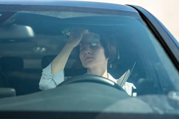 stock image Hot weather for drivers. Tired from heat woman in car cooling forehead with cold bottle of water. Exhausted female take break in car park suffering from heat in summer city feeling dizziness pressure