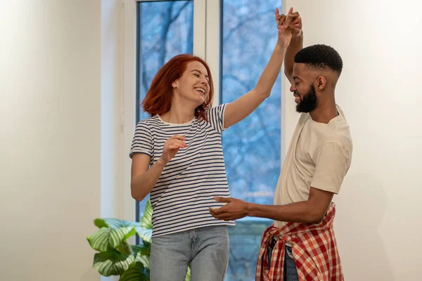 Young diverse couple in love preparing first wedding dance together, black man and caucasian girl dancing in living room, African guy teaching girlfriend how to dance during home date night