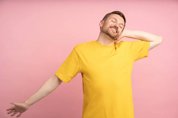 Happy well-rested man stretching smiling after good resting standing isolated on pink background. Satisfied relaxed bearded male with closed eyes. Good mood, optimistic life attitude, balance harmony.