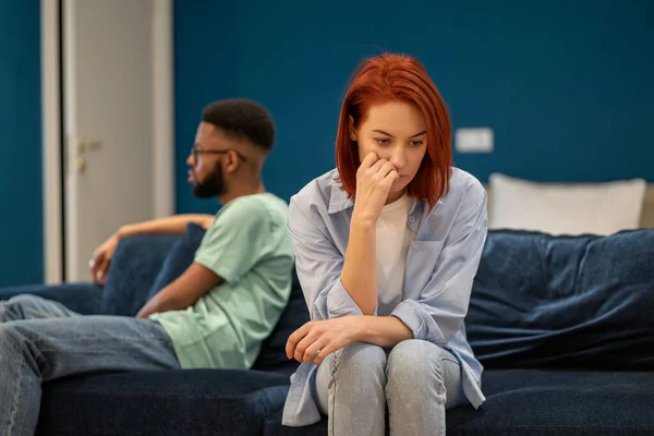Communication problems in marriage. Upset diverse family couple european wife and african american husband sit separately on sofa at home not talking after fight, having problems in relationships.