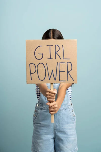Protester woman holding recycled cardboard with girl power slogan. Unrecognizable teenage girl feminist with empowerment sign isolated on studio blue background. Womens rights concept.