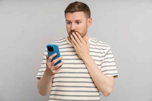 Shocked Scared Man Closing Mouth Hand Looking Smartphone Screen Grey — Stock Photo, Image