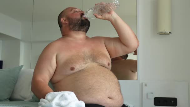 太りすぎの人は深呼吸し 水を飲んで シャワーがベッドに座った後めまいを感じます 脂肪質の男はタオルをこすり 自分自身を発作を通過しようとしています 過剰な体重 人々の健康問題の概念 — ストック動画