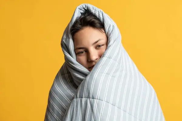 Sleepy teenage girl wrapped on blanket thinking about warm cozy bed isolated studio background. Pleased playful teenager schoolgirl before school in morning feel of security carefree childhood joy.