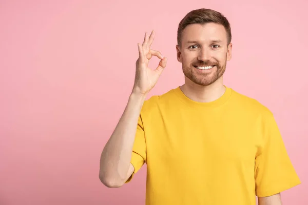 积极快乐的男人在粉色背景上展示出可以签名的手势 并在复制空间看着相机 广告横幅上的人物形象微笑的家伙 同意的象征 确认的概念 — 图库照片