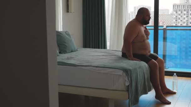 過体重の男性は発作が悪く ホテルの部屋でベッドに座っている呼吸が困難です 疲れた男がベッドに落ちる 心臓発作 脳卒中 過剰な体重の人々の健康問題の概念 — ストック動画