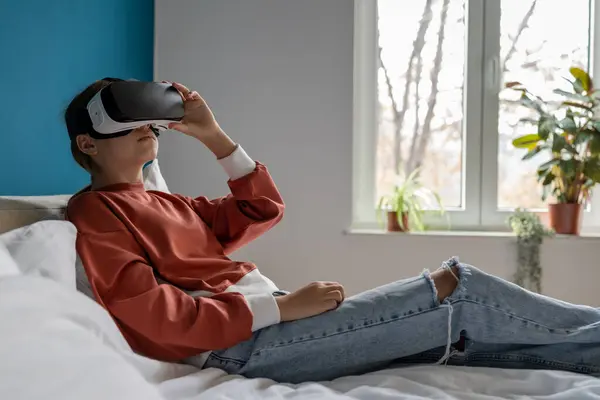 在Vr眼镜中看到360度浸入式教育视频的十几岁的女孩得到了释放 戴Vr护目镜的妇女使用横向耳机躺在床上 虚拟现实 儿童与教育 — 图库照片