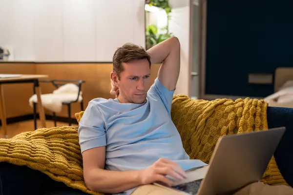 stock image Tired serious frown man workaholic working on laptop at home lying on couch looking at screen. Overworking, overjob concept. Typing texting reading documents, chatting online. Freelance, remote work.