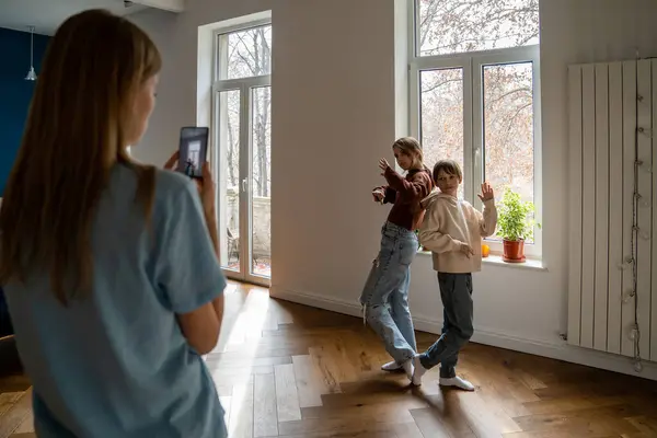 Family of three mother and two kids making social media content video on smartphone, modern young mother recording children bloggers dancing in front of phone at home. Blogging and small children