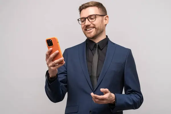 Smiling male businessman with smartphone. Happy successful man with mobile phone makes online electronic transaction merchant trader concludes lucrative contract on Internet, isolated on studio wall