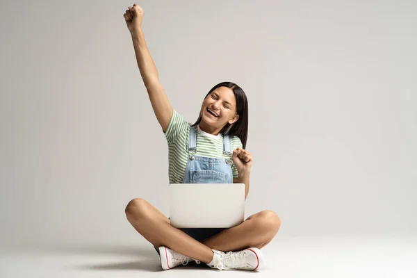 Szczęśliwy Uśmiechnięty Nastolatek Dziewczyna Raduje Siedząc Szarym Tle Laptopem Nogach — Zdjęcie stockowe