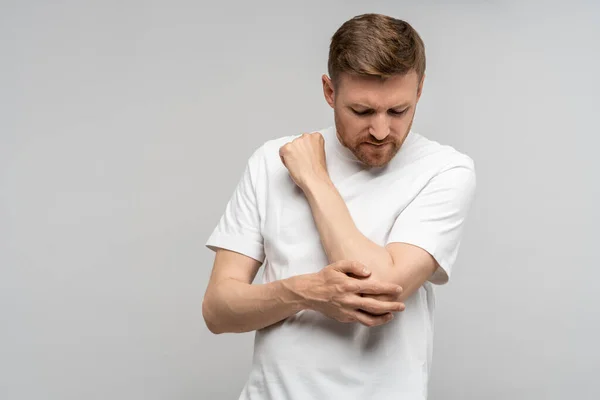 stock image Man touching hand elbow feeling pain isolated on gray background after injury. Neuralgia, pinched nerve in arm after injury, broken fracture bruised hand. Health problems, bad symptom, hurt concept.