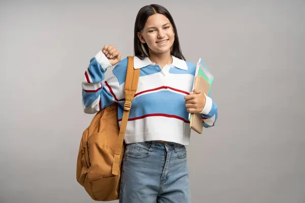 积极的学生少女喜欢灰色的背景 带着背包和教育笔记本看着相机 形象笑容可亲的黑发少女穿休闲装 大学学习概念 — 图库照片
