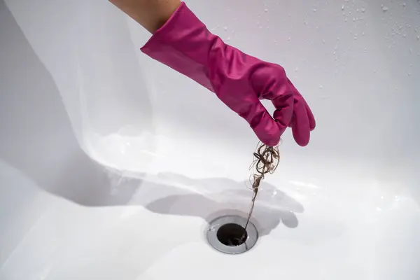 Hand pulls hair out of bathroom drain. Palm in purple latex glove removing shock of hair from siphon. Sink clogged with disgusting hair. Cleaning bathroom sewer trap. Close up. Hair loss problems.