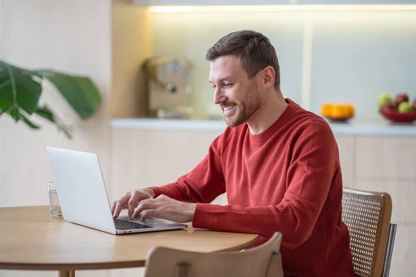Friendly smiling sales man working at laptop computer at home, messaging, typing, having video call. Optimistic positive male looks like freelancer sales manager, marketer, IT programmer, developer