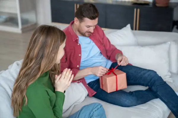 Happy Man Sitting Sofa Cardboard Gift Box Trying Unbrace Red — Stock fotografie