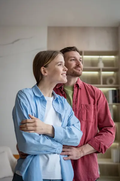 stock image Romantic loving man and woman looking at window in contemplation, hugging with fondness, love and affection, smiling. Married couple of wife and husband dreaming of happy family life, future, children