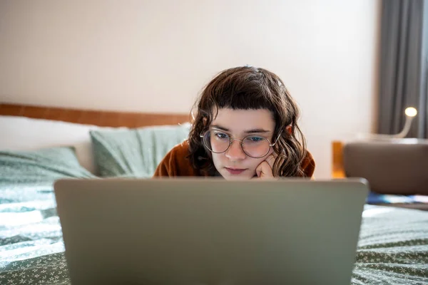 興味をそそられた集中した深刻な十代の少女は週末 家で休暇 ベッドに横たわり 面白い映画を見たり ビデオを見たり ラップトップコンピュータで映画をリラックスしたり 注意深くオンラインブックを読む — ストック写真