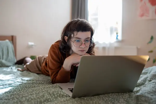 興味深い集中10代の少女はベッドに横たわり 興味深いフィルムを見たり ビデオを見たり ラップトップコンピュータ上の映画を観たり オンラインブックを注意深く読んだり 週末に働いた後にリラックスしたり 休暇を過ごしたりします — ストック写真