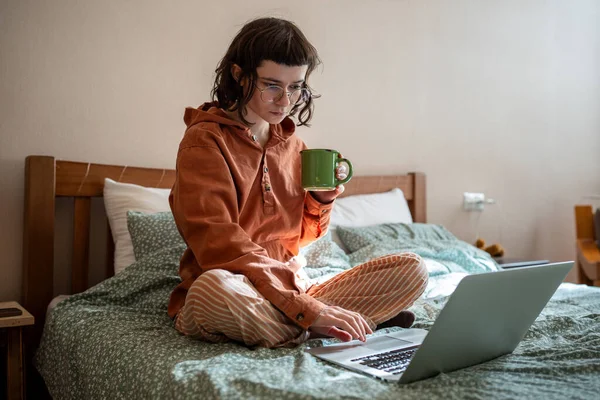インテリジェントな10代の少女は ノートパソコンから注意深くテキスト文書を読み 考えます ティーンガールは紅茶のカップでベッドに座っている ホームスクール 遠隔オンライン教育コンセプト — ストック写真