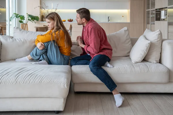 Annoyed ignoring woman sitting on sofa apathetically looking at window with blank stare demonstratively neglecting excusing, justifying man. Misunderstanding, confrontation, crisis in family life