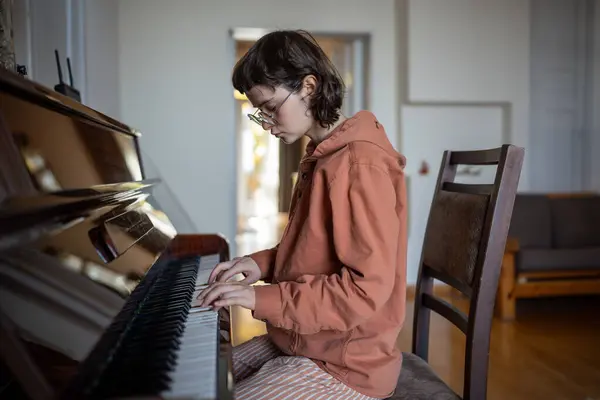 stock image Teenager sitting on chair, playing piano, improvising, practicing skills at home lesson, learning instrument notes, performing classical music for meditation, relaxation, as sound therapy and hobby