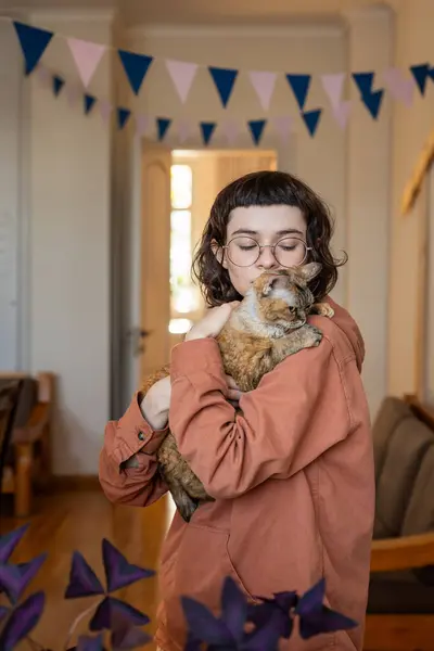 Woman cat lover hugging kissing curious naughty pet holding in hands at home. Affectionate girl in glasses petting kitty. Friendship between people animals concept. Girl closing eyes with pleasure.