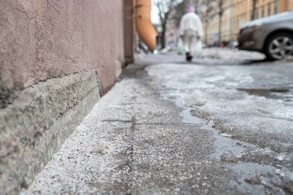 Technical salt grains on icy sidewalk surface in wintertime, used for melting ice and snow, person on background. Applying salt to keep roads clear and people safe in winter weather from ice or snow