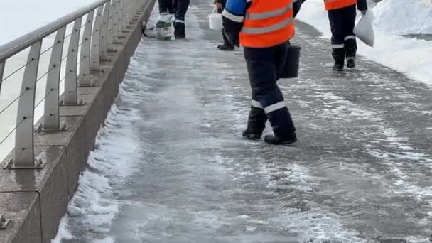 把盐撒在拖鞋人行道上的工人 冬季道路处理用除冰试剂 防止在路上滑倒 把技术盐撒在铺路板上 以清除冰和防止滑倒事故 — 图库视频影像
