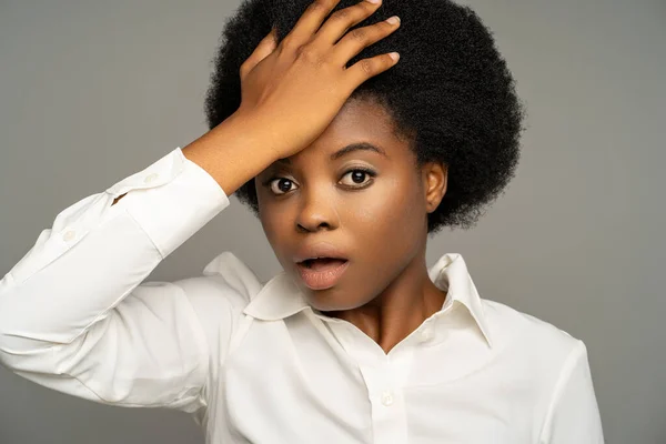 Stock image African american female remembering forgotten important task, punching in forehead, dropping jaw, having stunned puzzled excited face expression. Black woman in white office blouse on grey background