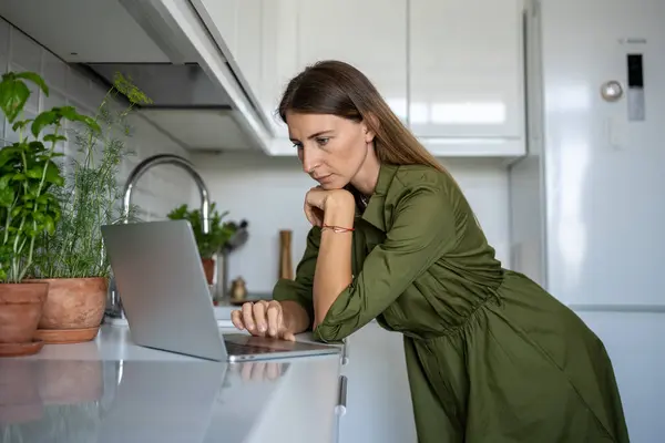 有兴趣的女人在厨房做饭的时候 会查看笔记本电脑屏幕 选择看电影 在互联网 社交网络 网页上浏览食物食谱的女性为重点 — 图库照片