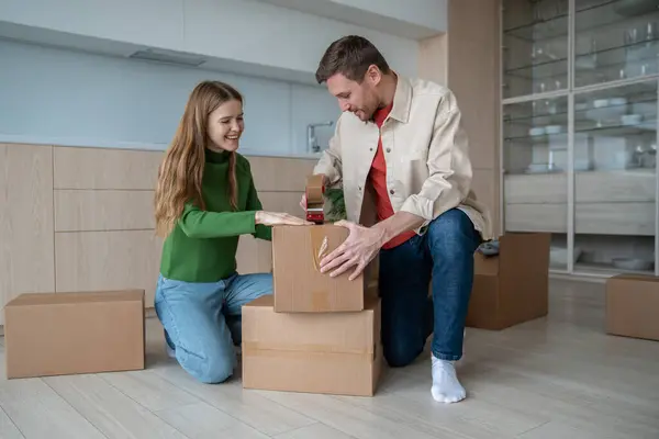 Joyful boyfriend and girlfriend excitedly preparing to move new place. Couple carefully packs things into cardboard boxes, trying not forget anything. Man and woman looking forward to new home moving.