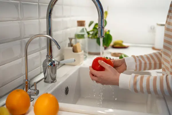 Woman hands washing fresh red peppers paprika in home kitchen for salad. Natural organic ingredients for healthy vitamins eating. Pleasure from vegan raw cuisine. Cleanse to vegetables and fruits