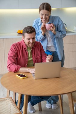 Happy family pleased man and woman smiling excitedly booking air tickets on internet app using laptop. Delighted couple is looking to screen computer together online shopping with credit card in hand. clipart