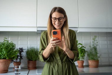 Akıllı telefondan gülümseyen mutlu ve rahat bir kadın evde internet iletişiminin tadını çıkarıyor. Milenyum kadınının arkadaşlarıyla cep telefonuyla sosyal medyada sohbet etmesine memnun oldum..