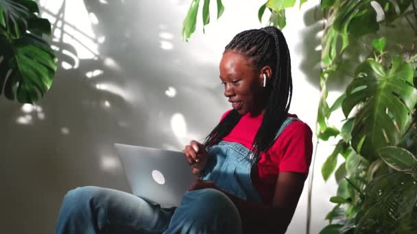 이어폰을 흥미로운 아프리카계 미국인 여성은 노트북과 무릎을 이야기하고 친구와 통화에 — 비디오