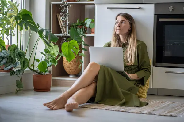 坐在膝上型电脑旁 心不在焉的女人焦急地看着窗外思考着问题 忧心忡忡的女性缺乏精力 在家里的地板上思考着自由职业的任务 — 图库照片