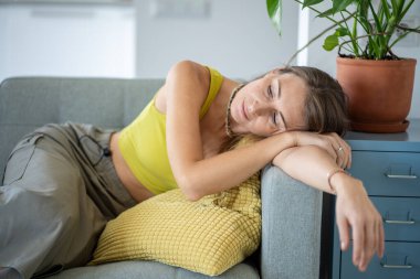 Weary Scandinavian female resting lying on couch daydreaming at home. Pensive tired woman relaxing leaning on armrest of sofa thinking about future. Mental health, stress relieve, procrastination. clipart
