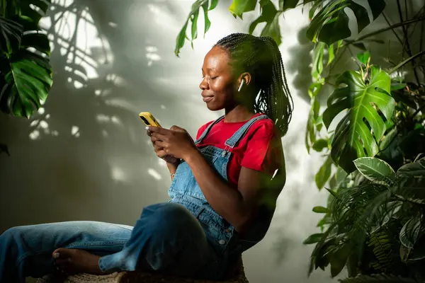 Χαλαρωμένη Αφροαμερικανή Γυναίκα Φορούν Ακουστικά Κοιτάζει Οθόνη Smartphone Απορροφάται Επιλέγει — Φωτογραφία Αρχείου